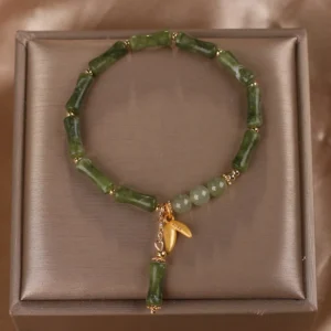 Overhead view of bamboo jade beaded bracelet with gold metal connectors and bamboo drop pendant in velvet tray