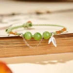 Sterling silver bamboo leaf charm jade beaded bracelet flat lay on vintage book showing green hetian jade beads and braided rope