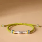 Sterling silver bamboo jade bracelet with yellow-green braided cord and jade bead toggle, flat lay top-down view