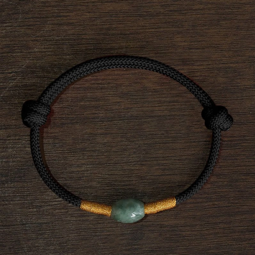 Black cord jade protection bracelet flat lay top-down on dark wooden desktop showing black braided cord with gold accents and jade bead
