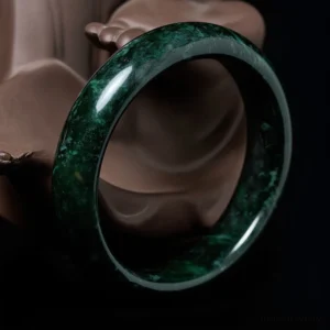 Hand-carved jade bangle three-quarter overhead angle displaying wide polished band with glossy dark green finish and natural stone texture