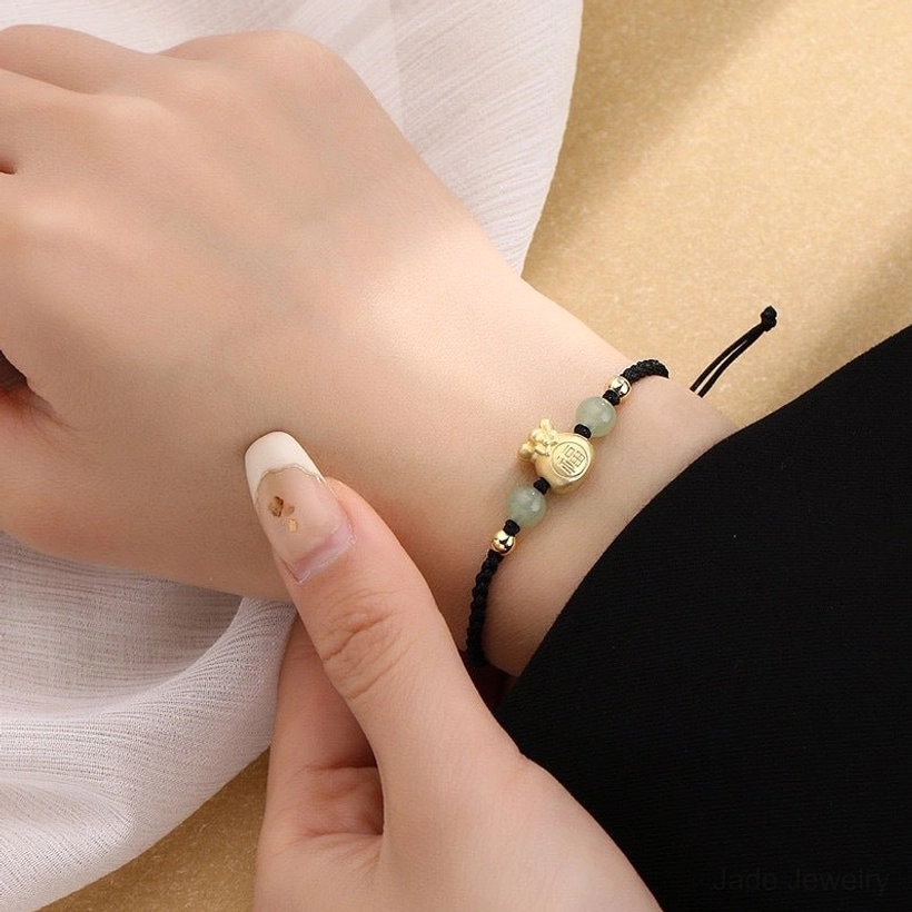 Black rope jade prosperity bracelet close-up wear view on wrist showing braided rope construction, gold charm, and natural jade beads on soft fabric background