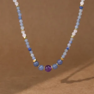 Close-up flat lay of blue aventurine jade necklace on kraft paper background, featuring central amethyst bead with gold metal accents