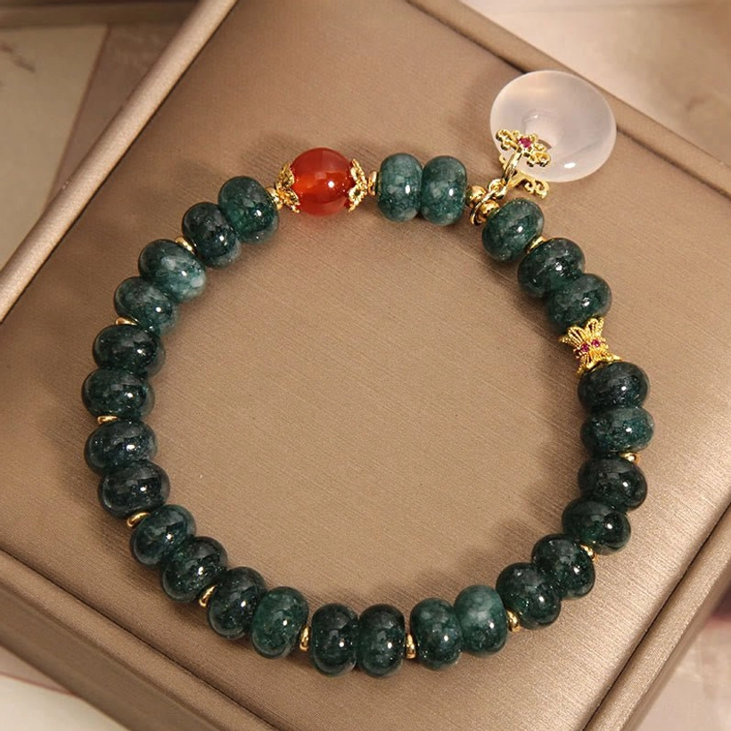 Diagonal side view of blue jade prosperity bracelet in storage box, displaying peace buckle talisman and bead arrangement