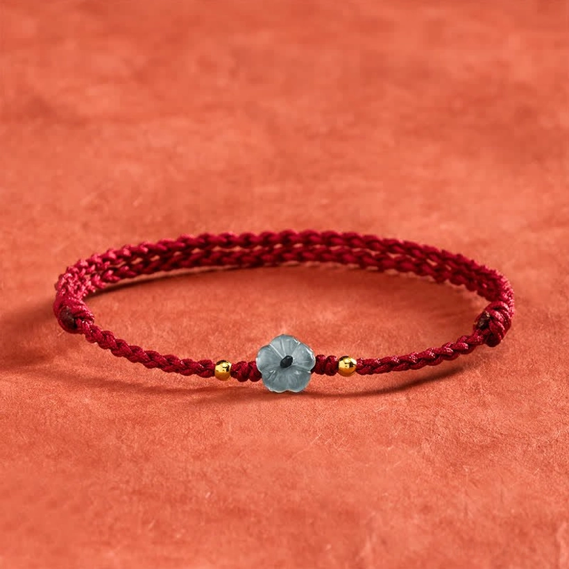 Blue jade flower red string blessing bracelet overhead view with burgundy braided cord and gold spacers on terracotta textile