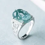 Blue jade Pixiu fortune ring with 925 sterling silver hollow coin band, three-quarter top view showing intricate jade carving and silver detailing