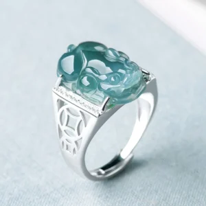 Blue jade Pixiu fortune ring with 925 sterling silver hollow coin band, three-quarter top view showing intricate jade carving and silver detailing