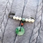 Bodhi seed jade peace buckle brooch with white jade beads and green jade pendant on grey cable-knit sweater