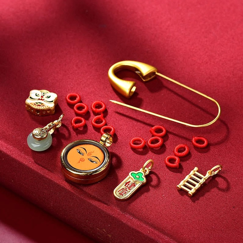 Loose brooch components showing gold charms, red cord loops, enamel pendants, and safety pin hardware