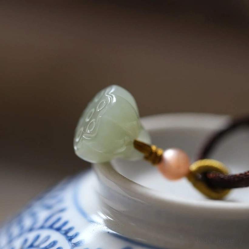 Carved lotus jade pendant with brown cord and golden decorative knot on porcelain, side close-up