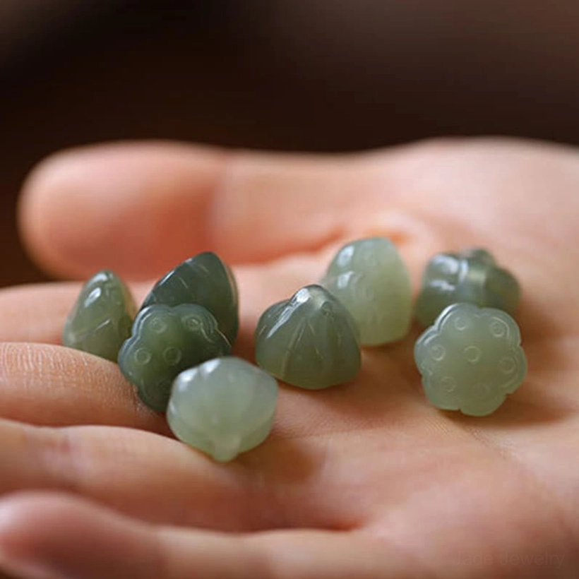 Multiple carved lotus jade pendants in matte light green, overhead palm display