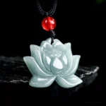 Light celadon carved lotus jade prosperity pendant necklace with black cord and red bead, front flat view on stone display