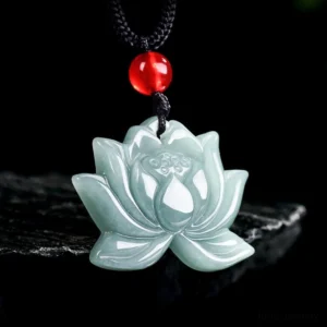 Light celadon carved lotus jade prosperity pendant necklace with black cord and red bead, front flat view on stone display