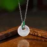 Chalcedony peace buckle bamboo leaf necklace pendant with white stone and green enamel bail, front view on wooden tray with water reflection