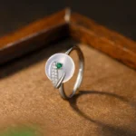 Adjustable chalcedony bamboo leaf ring front view with white stone, green inlay, and zircon accents on wooden surface