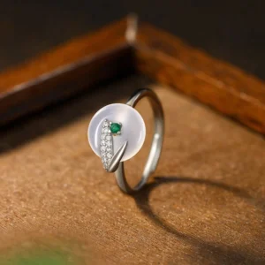 Adjustable chalcedony bamboo leaf ring front view with white stone, green inlay, and zircon accents on wooden surface