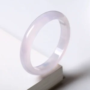 Translucent lavender chalcedony bangle displayed on wooden block, three-quarter side view showing smooth polished surface and glossy finish