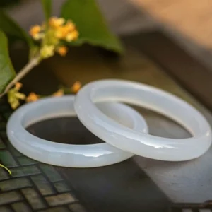 Two natural chalcedony bangles flat lay from above, milky white polished finish on decorative green tile with yellow flowers