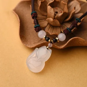 Overhead close-up of chalcedony fox charm necklace featuring green accent beads on wooden lotus ornament background