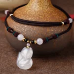 Chalcedony fox pendant necklace with braided brown rope and mixed crystal beads displayed on vintage pottery with bohemian styling