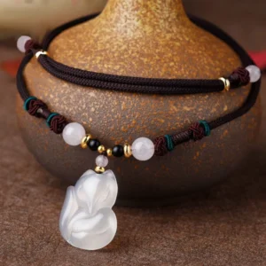 Chalcedony fox pendant necklace with braided brown rope and mixed crystal beads displayed on vintage pottery with bohemian styling