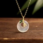 Gold-plated sterling silver chalcedony peace buckle necklace with bamboo leaf pendant, front overhead view on natural wooden surface