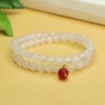 Natural chalcedony and red agate double-layer harmony bracelet with gold-plated charm, displayed on yellow desktop with book