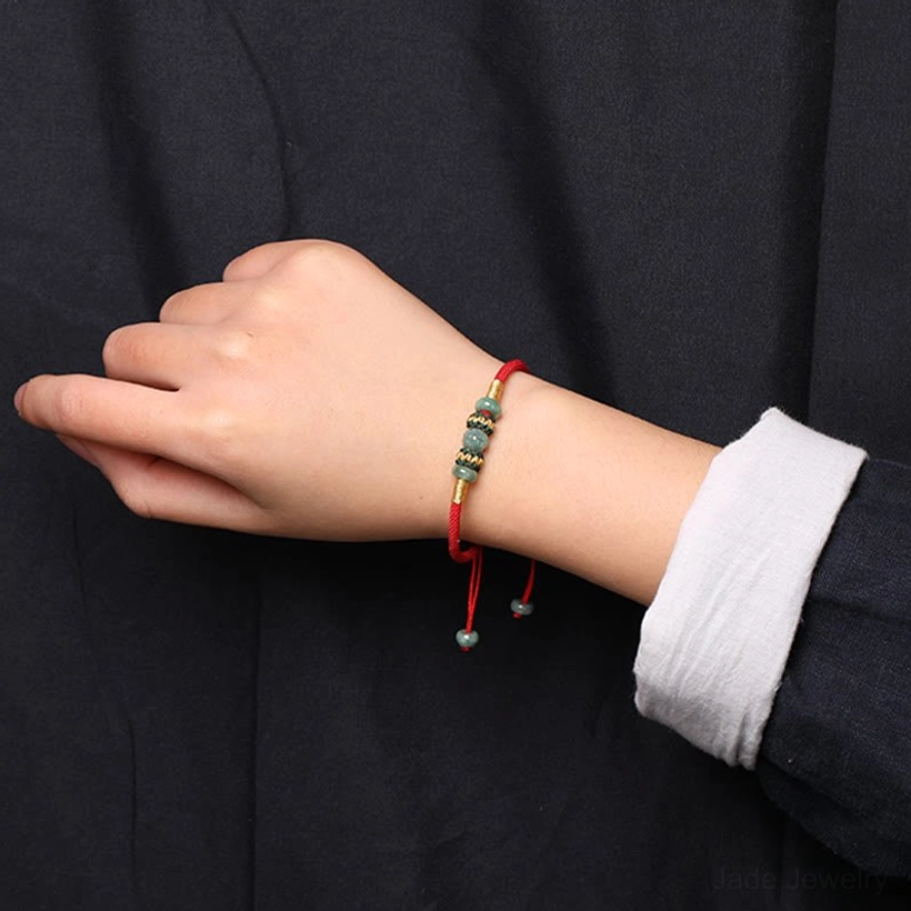 Slim jade prosperity bracelet on wrist showing compact bead set and adjustable red rope ends with dark formal shirt
