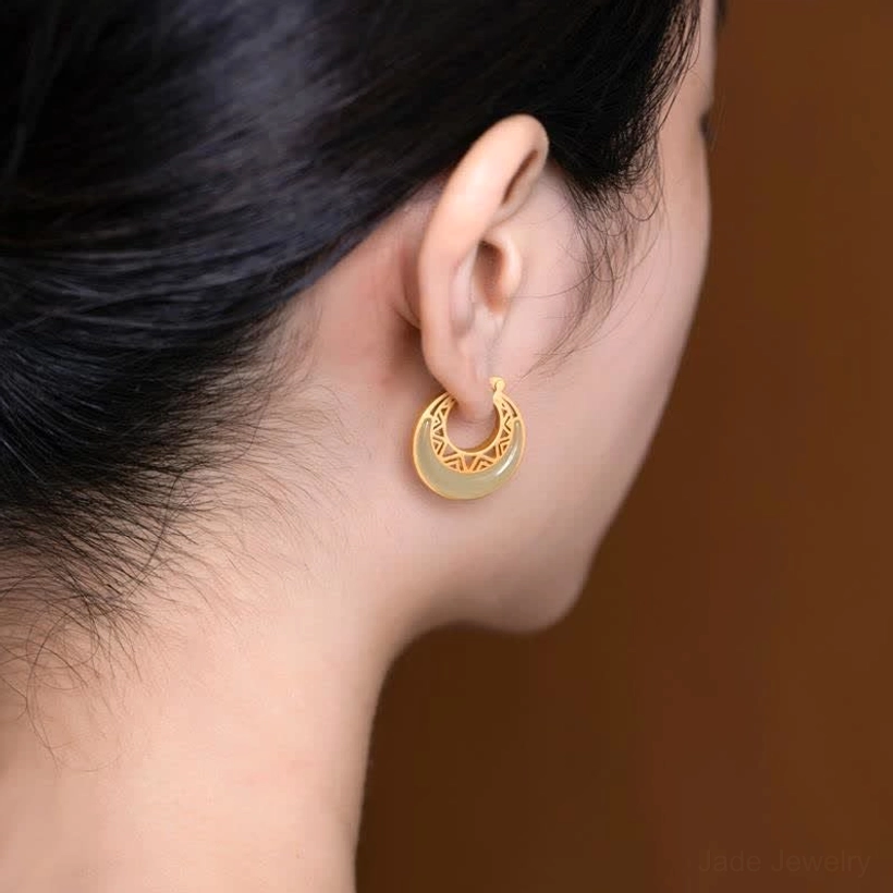 Detailed close-up flat lay of jade crescent earrings on blue fabric with golden bokeh background, showcasing hollow geometric pattern design