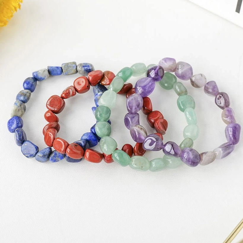 Three irregular natural stone crystal bracelets in blue, red, green, and purple tones flat lay on white background