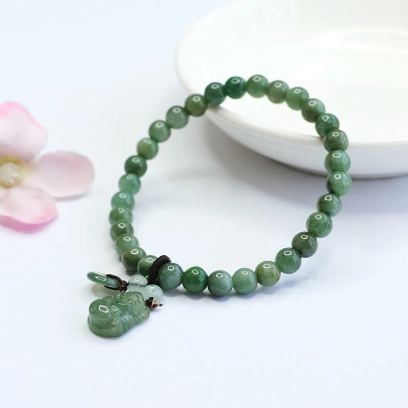 Smooth round cyan jade bracelet with Buddha pendant charm displayed in white ceramic bowl with pink flowers