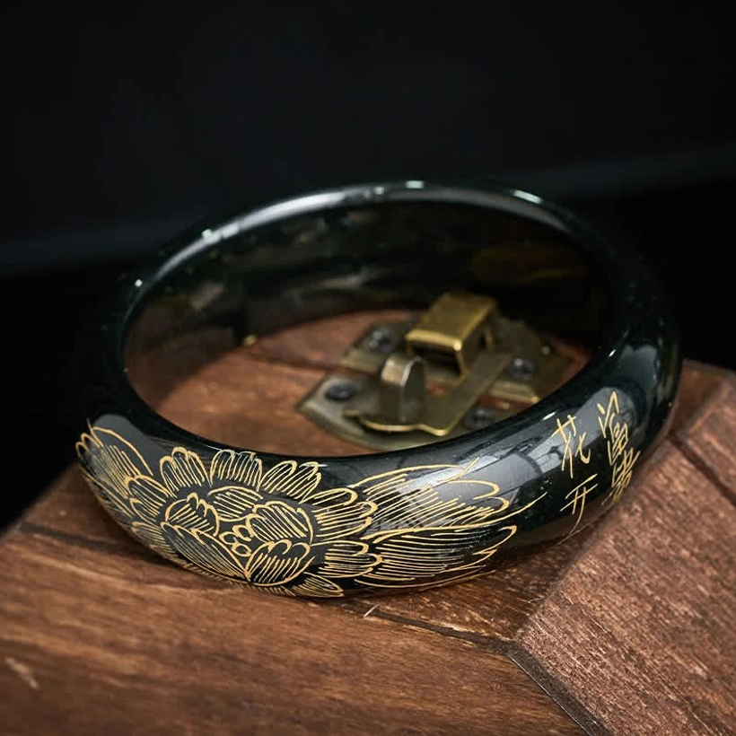 Natural cyan jade bangle with intricate calligraphy and flower carvings on wooden display stand