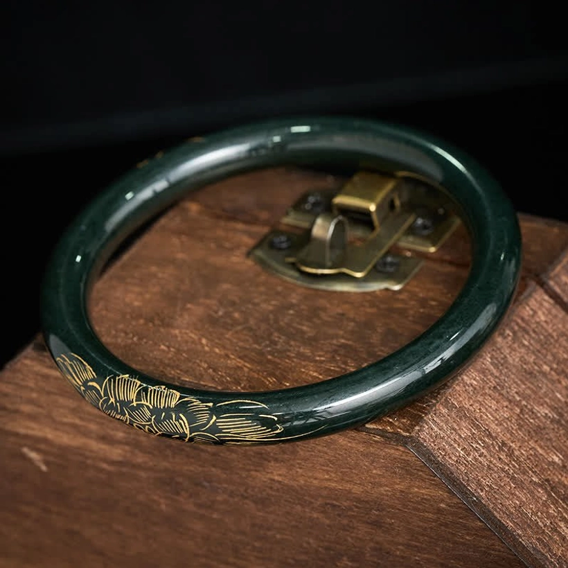 Handcrafted cyan jade bangle with gilded lotus koi design on vintage wooden storage display