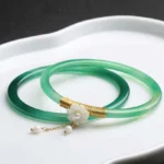Cyan jade bangle bracelet set with gold accents and pearl charm pendants displayed on decorative ceramic tray