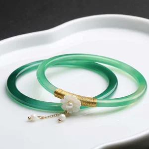 Cyan jade bangle bracelet set with gold accents and pearl charm pendants displayed on decorative ceramic tray