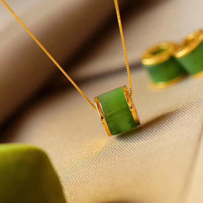 Dainty cyan jade barrel pendant necklace with green jade stone and gold trim, low-angle flat lay soft lighting