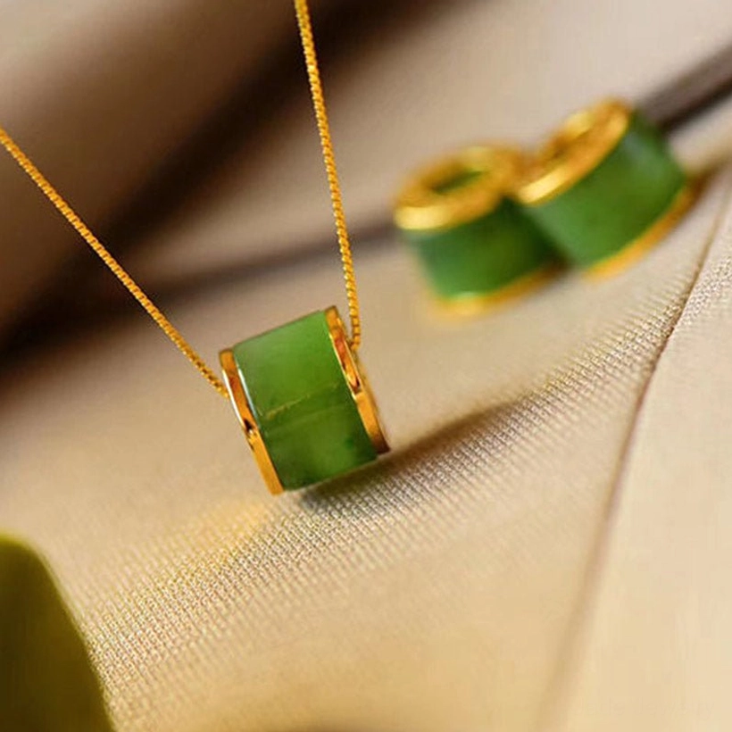 Polished cyan jade barrel pendant with gold box chain on khaki fabric, handmade jade necklace flat lay photography