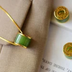Cyan jade barrel pendant necklace with gold trim, close-up top view showing polished jade stone detail on khaki fabric