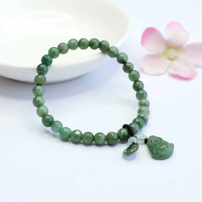 Cyan jade Buddha bracelet displayed in white ceramic bowl with pink flower arrangement, showing elastic string closure