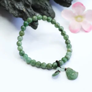 Natural cyan jade Buddha bracelet styled with decorative dark rock and pink flowers, showing detail of carved Buddha charm and accent jade beads