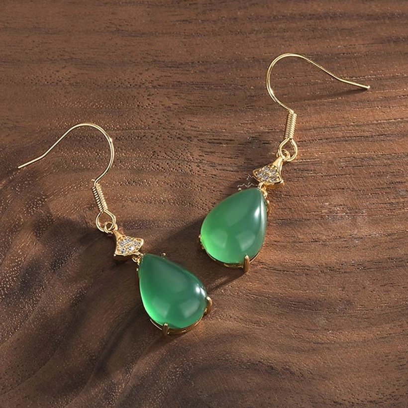 Paired cyan jade teardrop earrings placed side by side on wooden tabletop, eye-level frontal view showcasing the matching green jade stones and classic drop silhouette