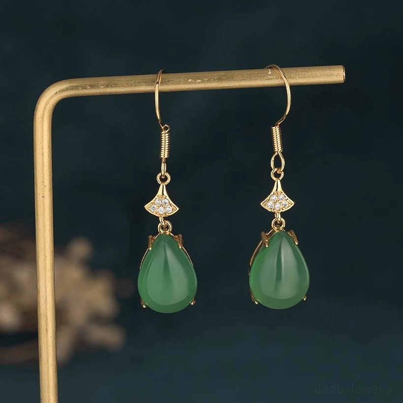 Cyan jade drop earrings on metal jewelry display stand with dark background, straight frontal view highlighting the polished teardrop jade stones and fan-shaped zircon connector detail