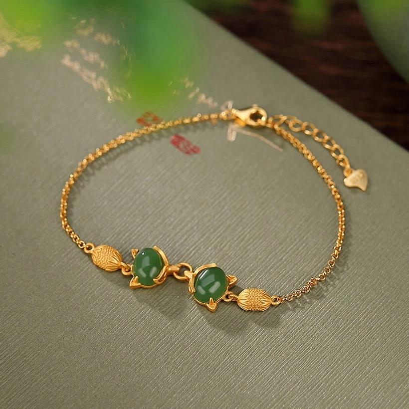 Cyan jade fox luck bracelet with sterling silver chain and gold-toned fox charm, overhead view on green calligraphy fabric