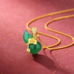 Cyan jade gourd lotus pendant necklace with gold chain on red background with golden glitter, featuring crystal-accented bail
