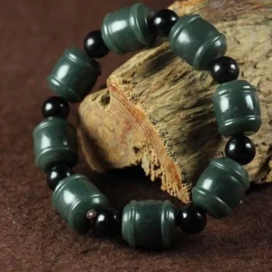 Natural cyan jade healing bracelet with barrel-shaped green beads and black spacer stones, displayed on weathered wood from three-quarter overhead view
