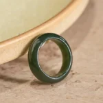 Cyan jade healing ring with polished glossy finish displayed on ceramic bowl rim, showing smooth solid band design from oblique angle