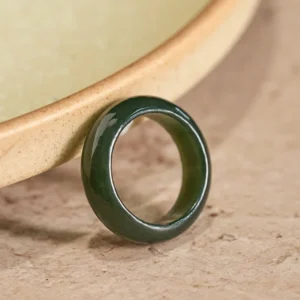 Cyan jade healing ring with polished glossy finish displayed on ceramic bowl rim, showing smooth solid band design from oblique angle
