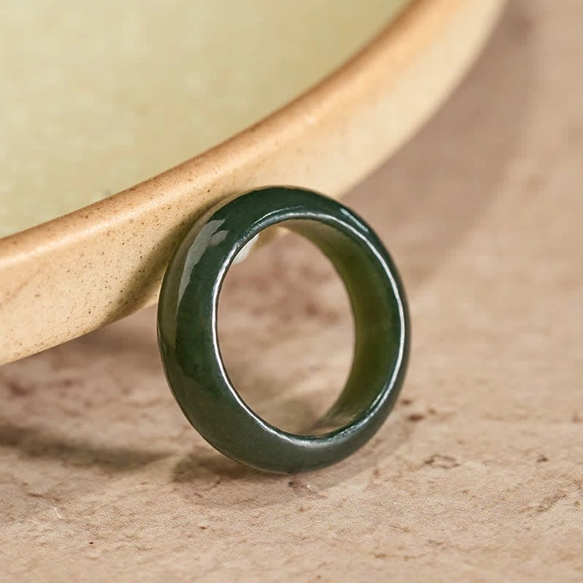 Cyan jade healing ring with polished glossy finish displayed on ceramic bowl rim, showing smooth solid band design from oblique angle
