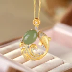 Cyan jade koi fish pendant necklace on pink velvet display, showing three-quarter view with gold metal accents and zirconia details