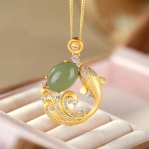 Cyan jade koi fish pendant necklace on pink velvet display, showing three-quarter view with gold metal accents and zirconia details